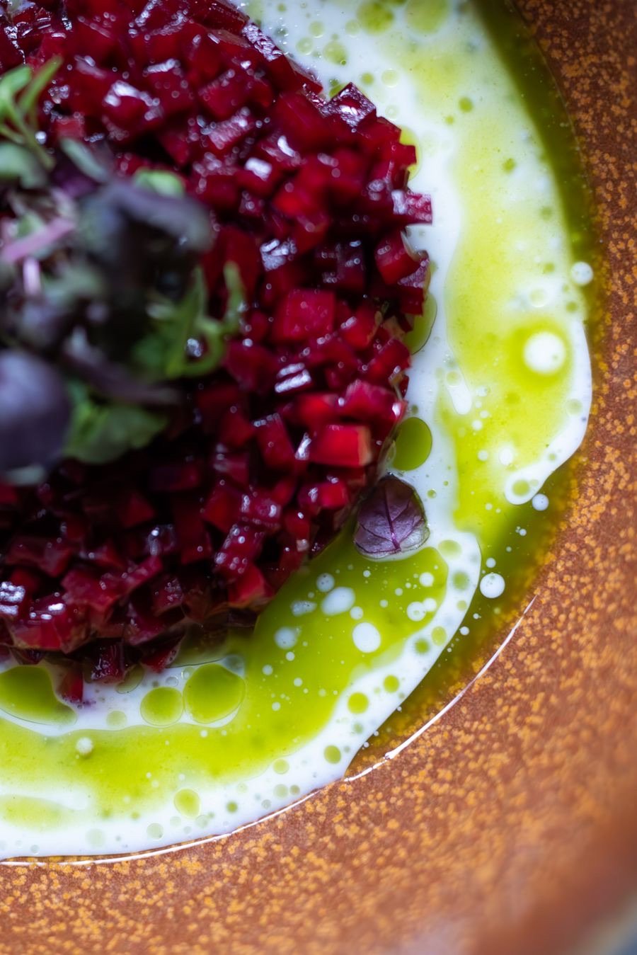 Remolacha en dados con aceite verde sobre un plato de cerámica cobriza.