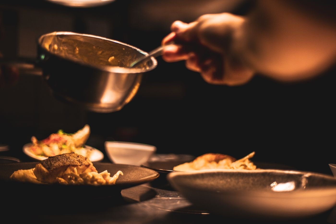 Manos de cocinero emplatando bajo una luz cálida en la cocina.