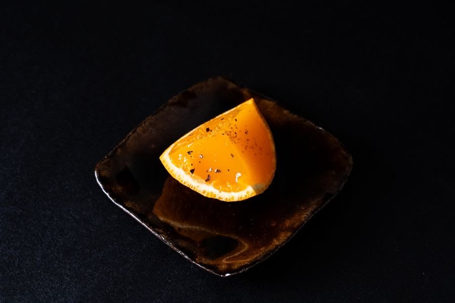 Gajo de cítrico sobre un plato oscuro de cerámica.