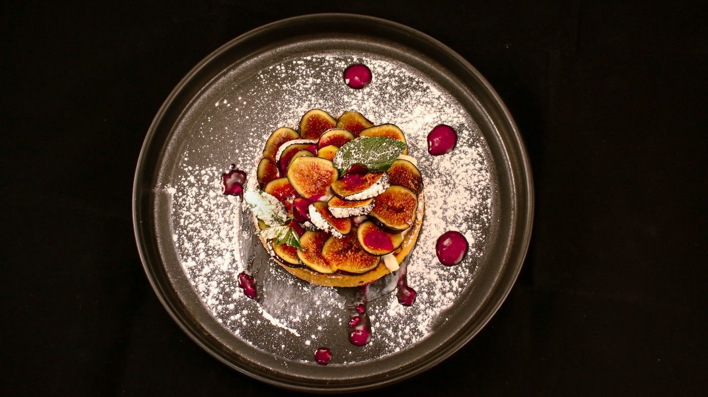 Tarta fina de higos con azúcar glas y gotas de frutos rojos.